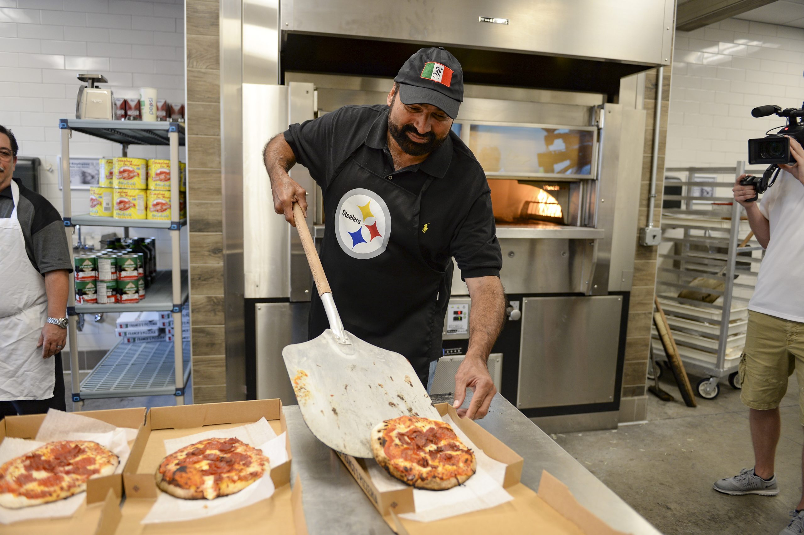 Steelers Legend and Hall of Famer Franco Harris sliding a fresh pizza into a box at Franco's Pizzeria at Acrisure Stadium.